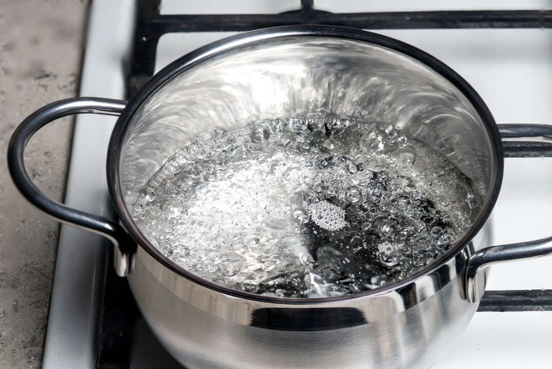 Water boils in a stainless steel pan on a gas stove.