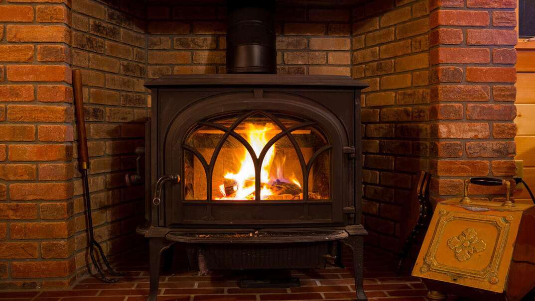 A cast iron wood burning stove is situated inside a red brick fireplace