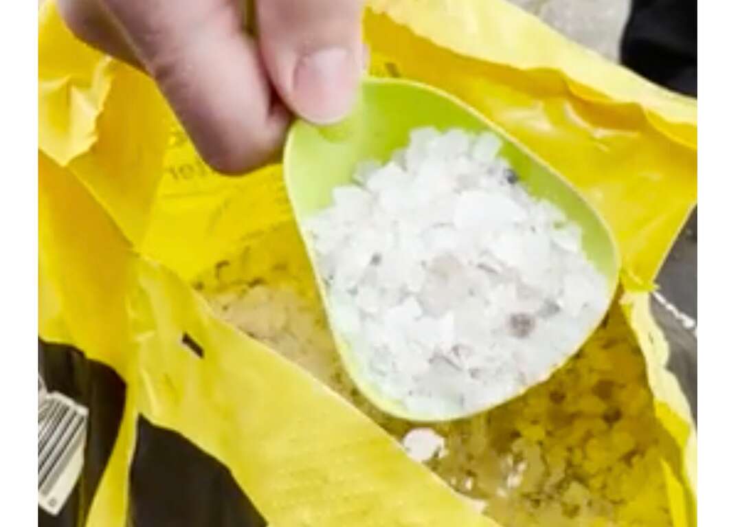 A man prepares to spread Ice Away brand rock salt from a yellow 50 pound bag