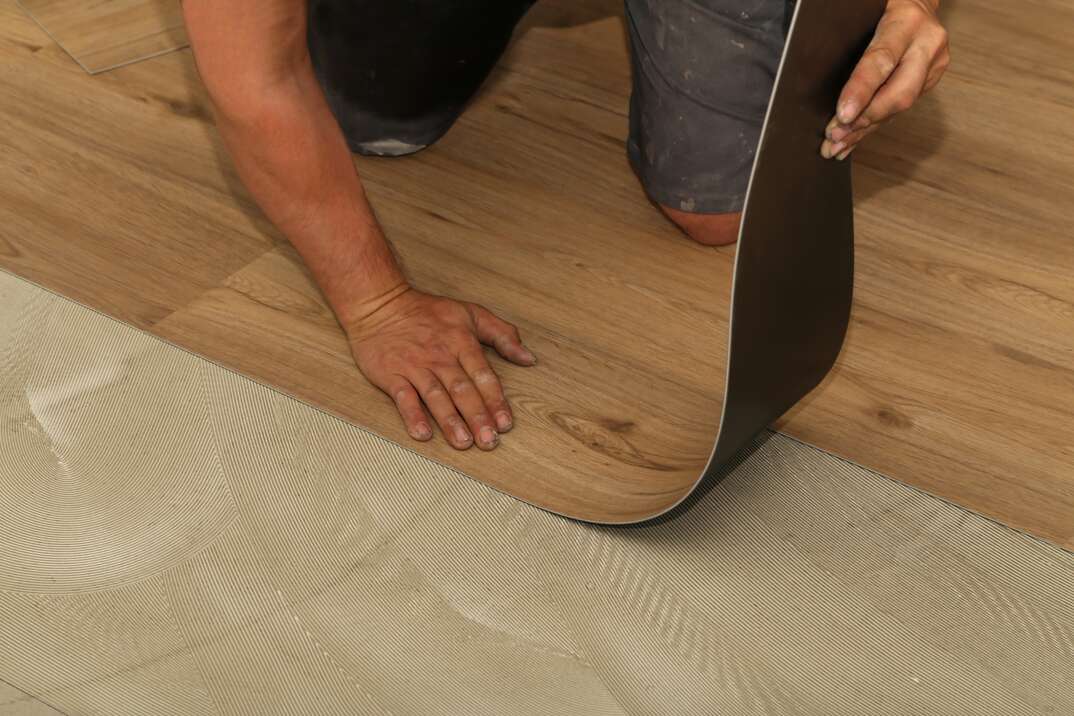 Male contractor installing new wood-styled vinyl tile floor