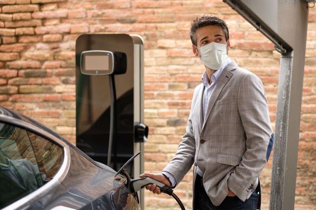 A businessman wearing a surgical mask is charging his Tesla using a wallbox EV car charger