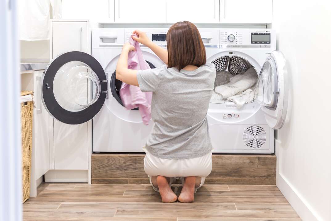 woman loading dirty clothes in washing machine for washing in utility room
