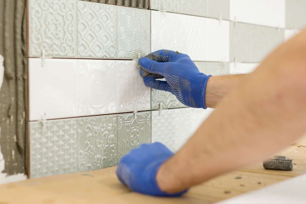 Placing tile spacers with hands on a kitchen backsplash being installed