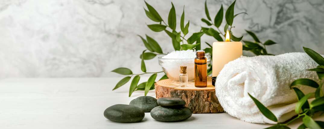 beauty treatment items for spa procedures on white wooden table  massage stones, essential oils and sea salt  copy space