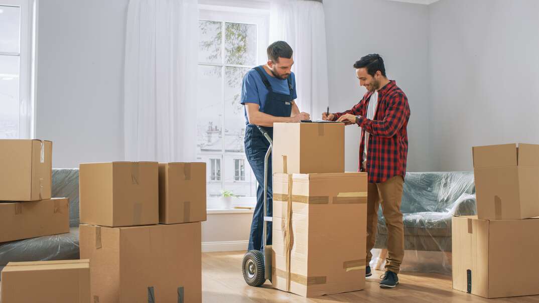 Happy New Homeowner Welcomes Professional Mover with Hand Truck full of Cardboard Boxes