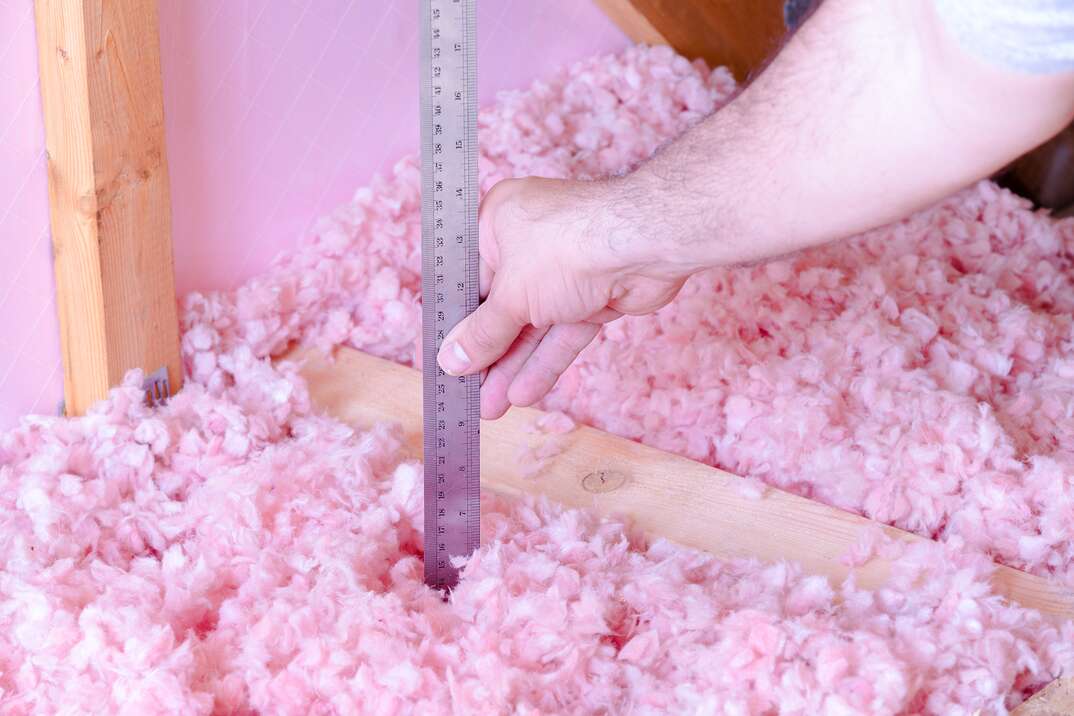 man is checking the energy efficiency of their house by measuring the thickness of fiberglass insulation in the attic