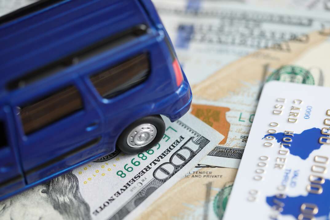 Close-up of credit bank card of holder and currency money. Blue toy vehicle and currency banknotes on table. Finance car insurance and business concept