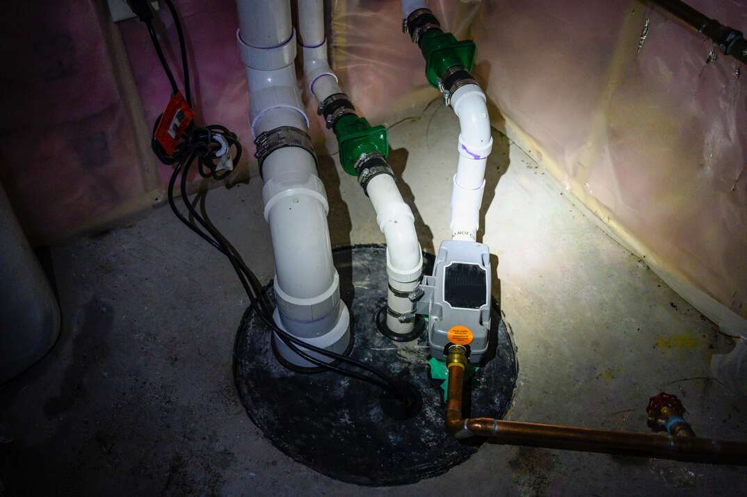 A fully installed sump pump is shown under a flashlight beam sticking out of a concrete basement floor with exposed pink insulation visible in the background, sump pump, pump, sump, basement, concrete floor, basement floor, flashlight, darkness, dark, insulation, pink insulation, exposed insulation, flooding, flood, flood control, flood prone, flood prevention, plumbing