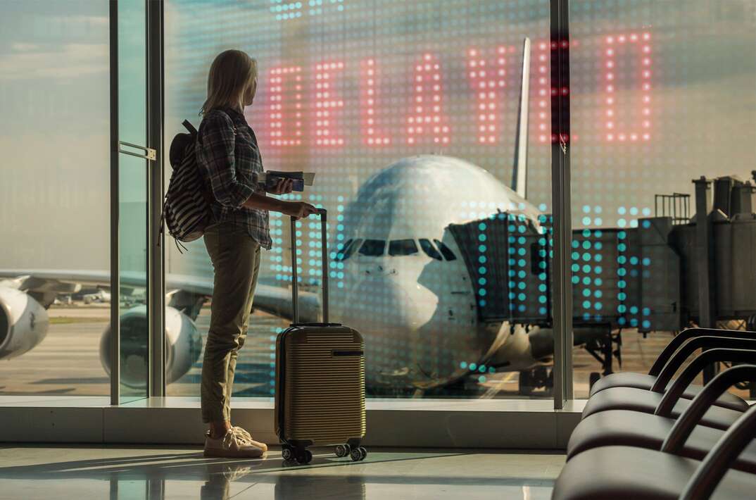 Woman stands in front of window at airport   delayed  sign is superimposed on the window