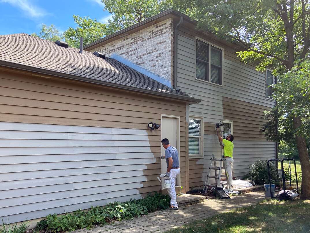 two men painting the side of a house