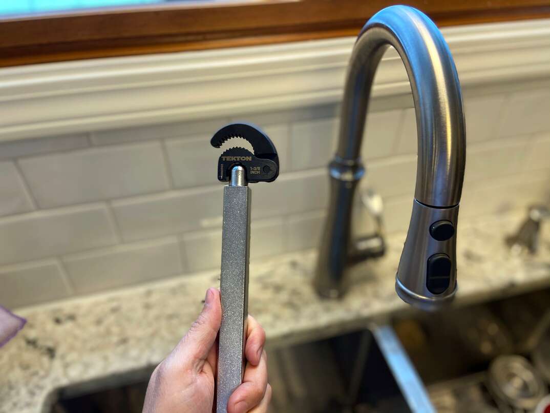 Photo of a man holding a basin wrench next to a kitchen sink 