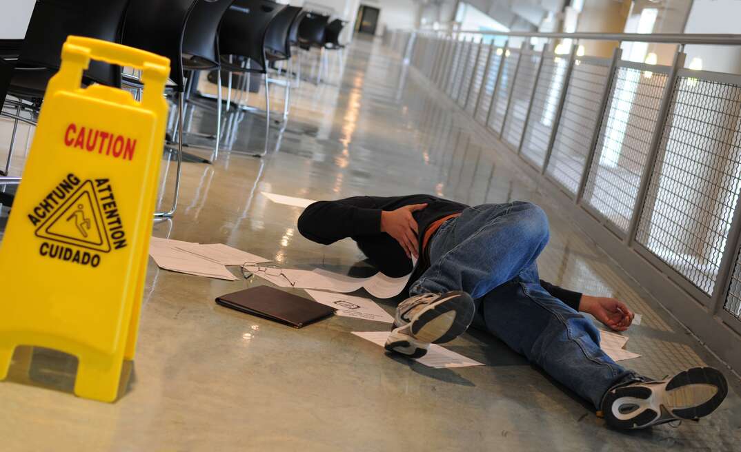 A man who slipped on a wet floor beside a bright yellow caution sign holds his back in pain..** Note: Shallow depth of field