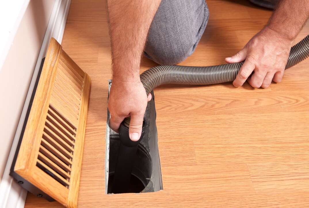 a man does a DIY Air Duct Cleaning with a vacuum 