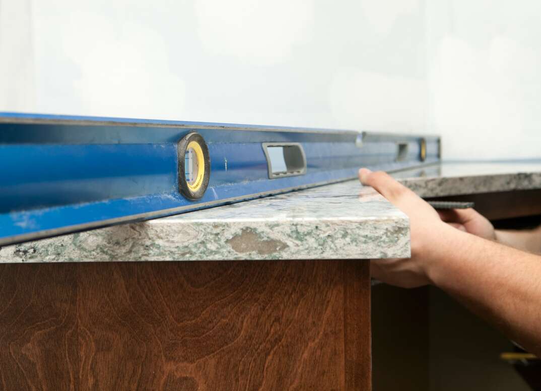 contractors use a level tool to properly adjust a new countertop as its installed