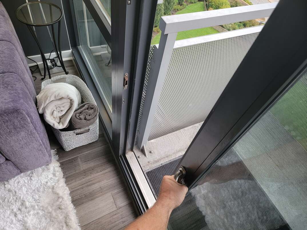 Human hand opening sliding glass door leading out to a balcony.