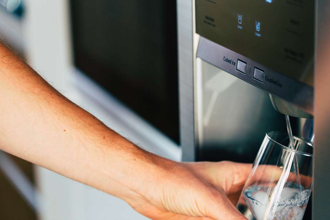 Male hand is pouring cold water and ice cubes from dispenser of home fridge 