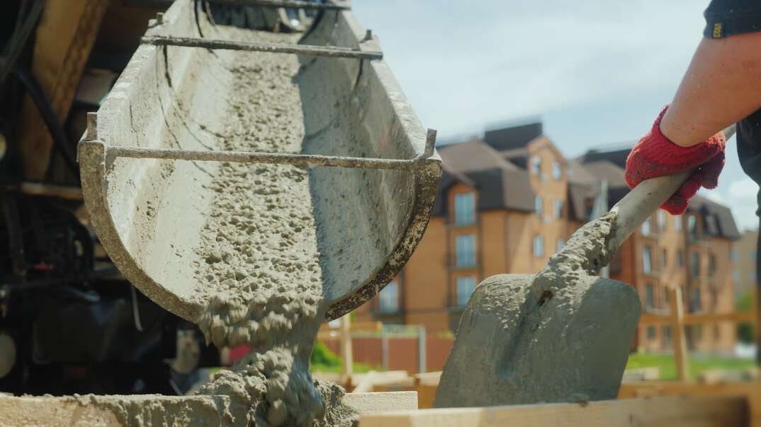 Building a cottage  Workers take concrete from a mixer into a wooden formwork