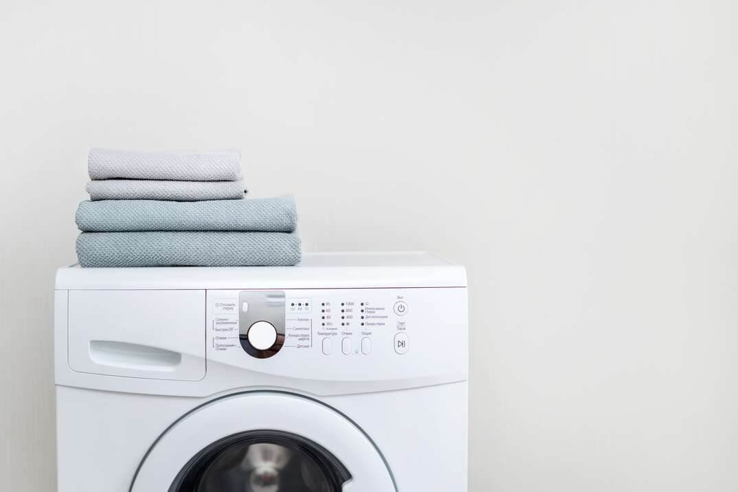 Washing machine on white background with fresh towels on top