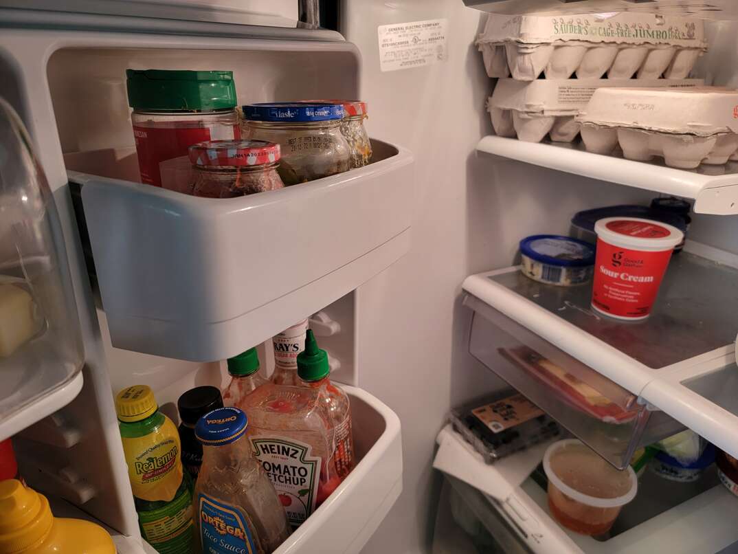 A refrigerator door is open to reveal food inside as well as where you can find the silver placard with the serial number and model number of the appliance.
