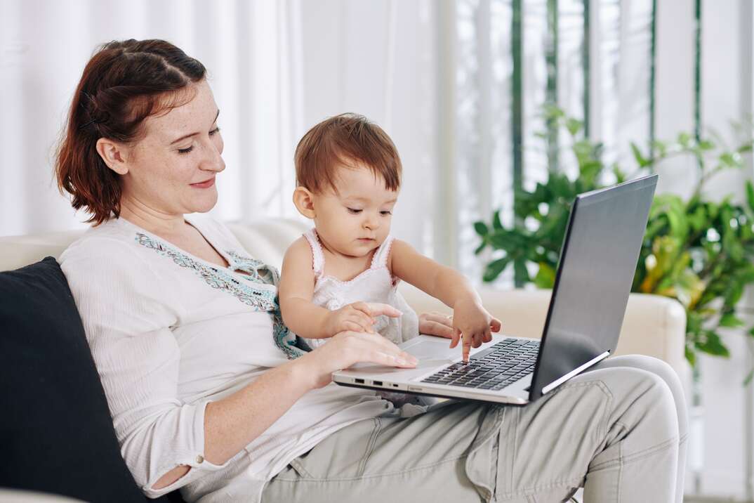 Smiling pretty young woman letting her daughter to push buttons on laptop