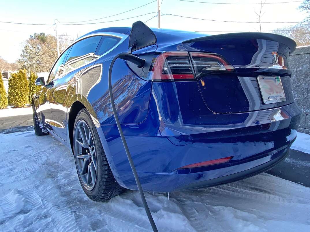 Blue 2018 Tesla Model 3 in a residential driveway getting charged 