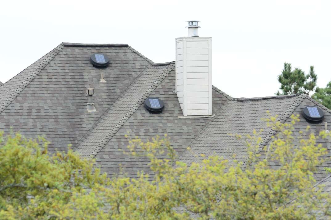 Solar Powered attic exhaust fans sit on top of a tall residential roof 