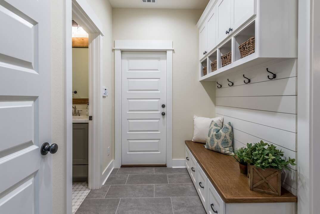 a modern white mudroom with a classif wood bench and shiplap on the wall