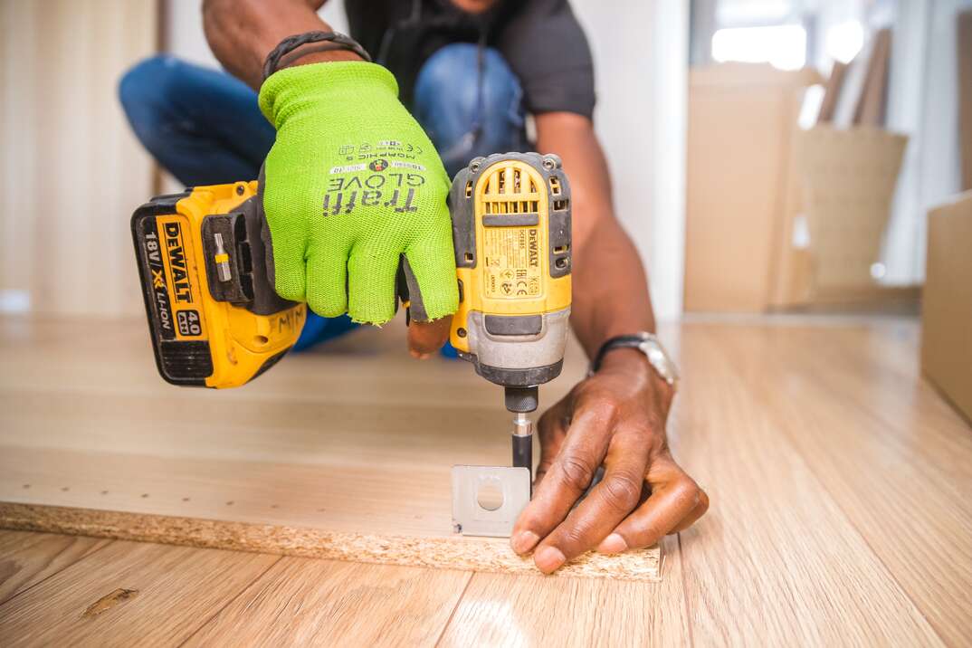 person kneeling on floor drilling into two pieces of wood