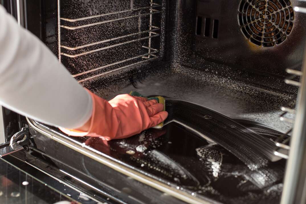 Person cleaning their residential oven with harsh chemicals and wearing red rubber gloves 
