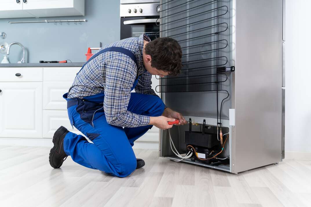 male appliance repairman working on the back of a refrigetor