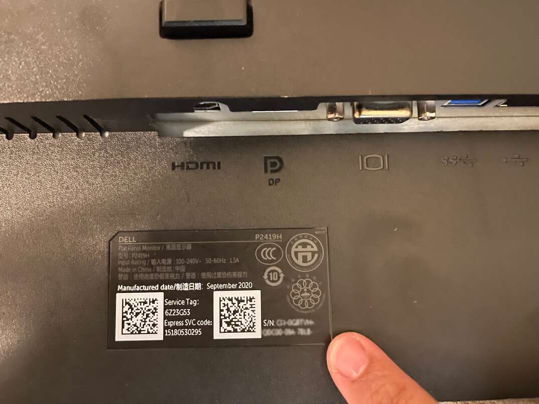 Finger pointing to the blurred-out serial number on the back of a black Dell computer monitor