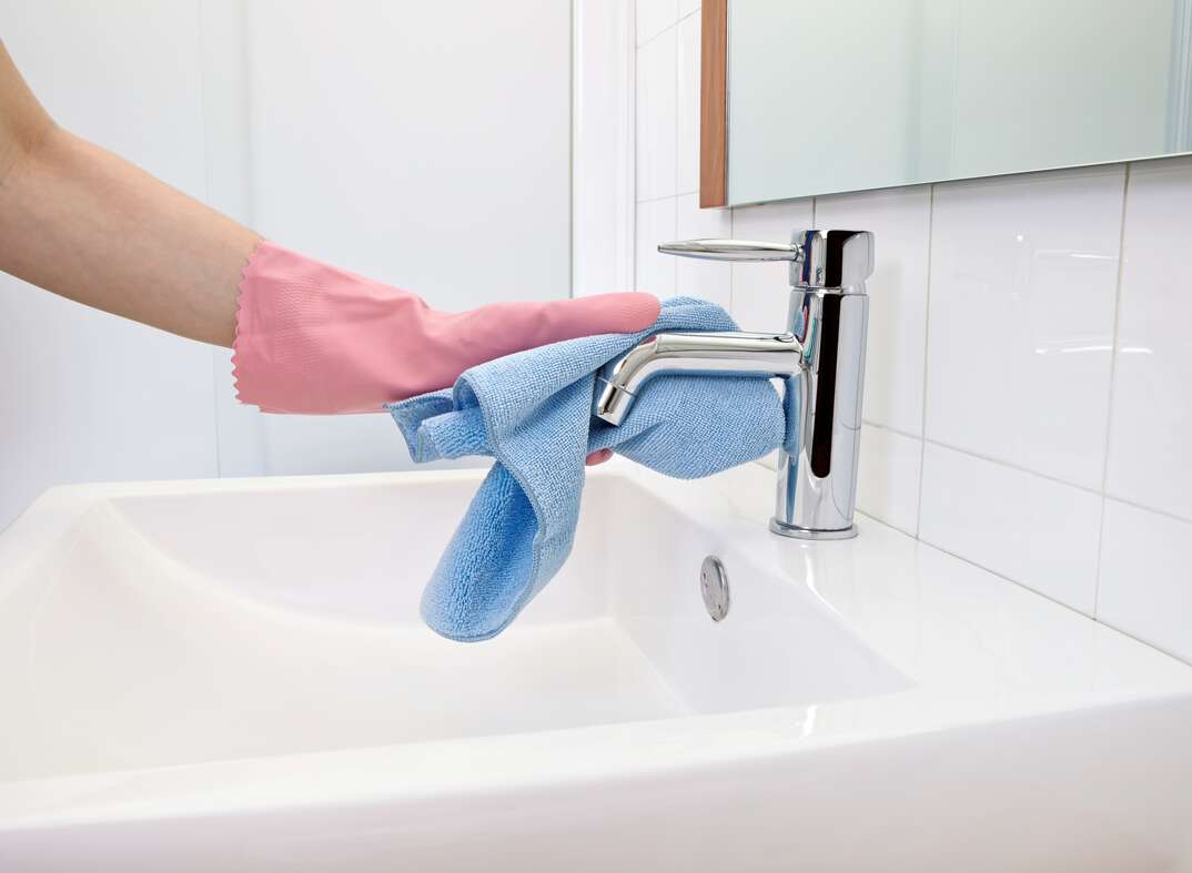 The woman, who is cleaning the faucet with microfiber cloth and gloves