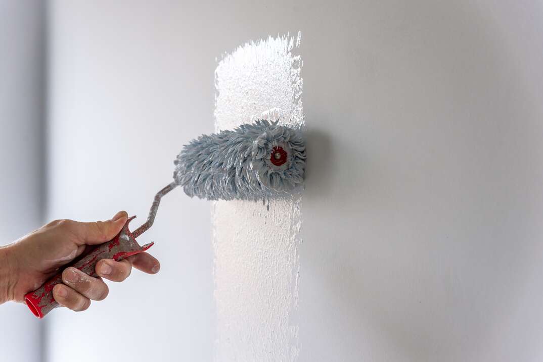 Painter Painting a House Wall with a Paint Roller.