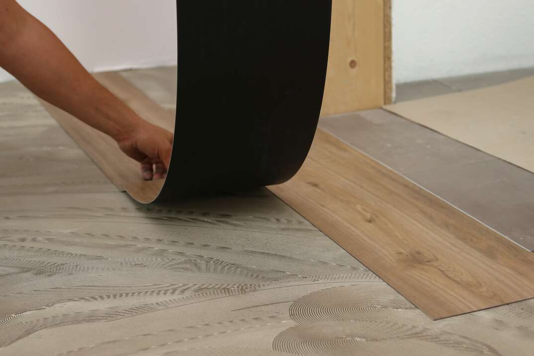 worker lays down sheets of vinyl or linoleum flooring that simulates a wood grain