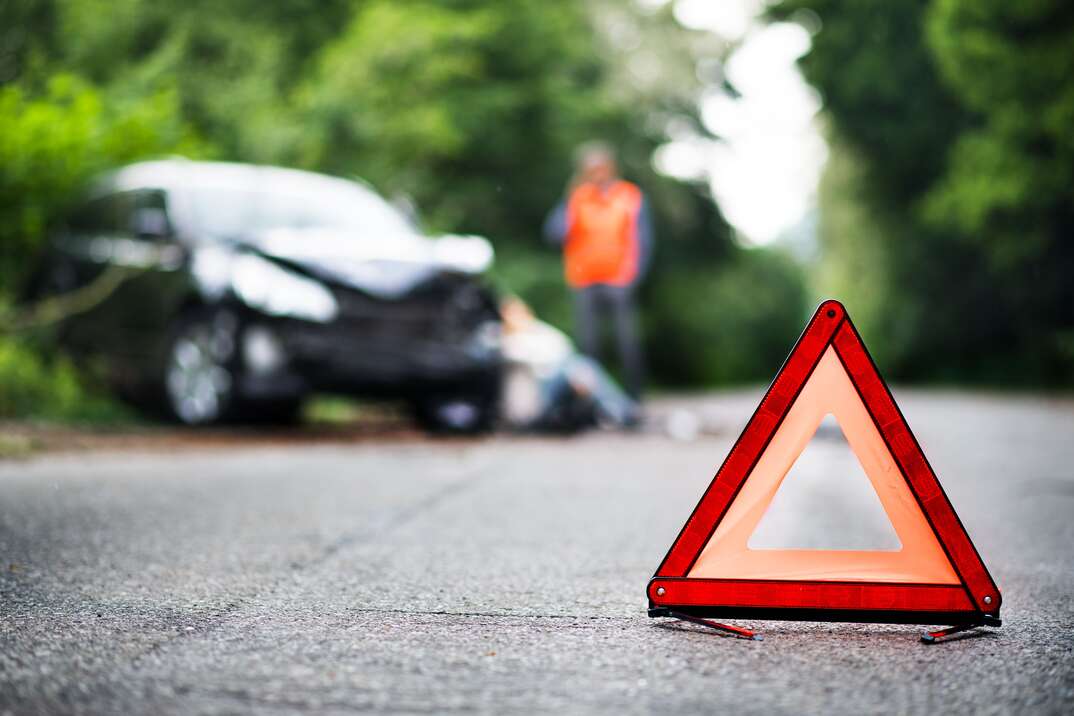 A close up of a red emergency triangle on the road in front of a damaged car and unrecognizable people. A car accident concept. Copy space.