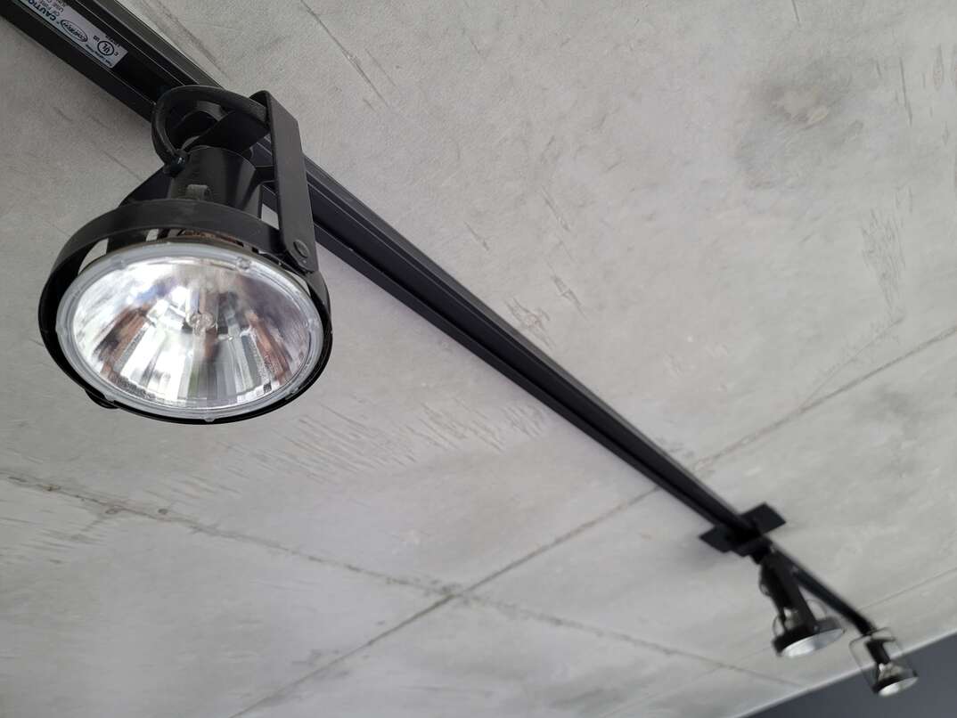 Black metal lighting track with three round spotlight-style lights pointing downward from gray exposed concrete ceiling
