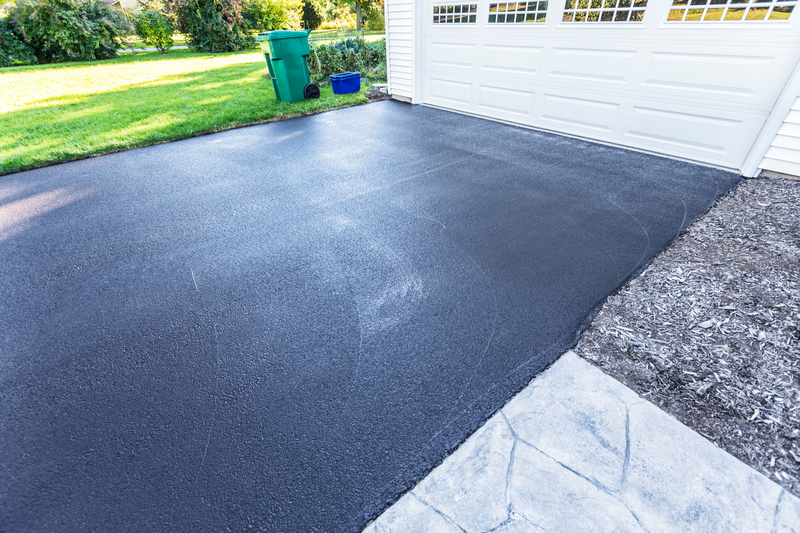 A fresh blacktop resealing job just finished on this asphalt driveway in a suburban residential district. The black sealant is still wet; needing at least 24 hours to dry.