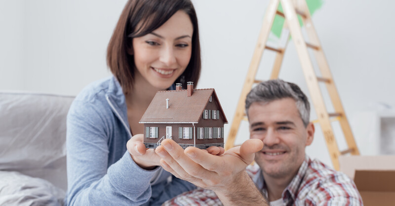 Happy smiling couple holding a model house, they are building their home together, real estate and construction concept