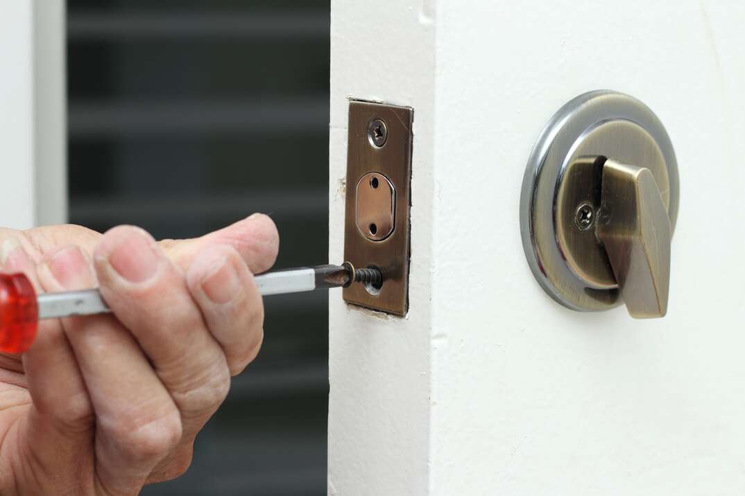 A worker is replacing the dead bolt on a home entryway door