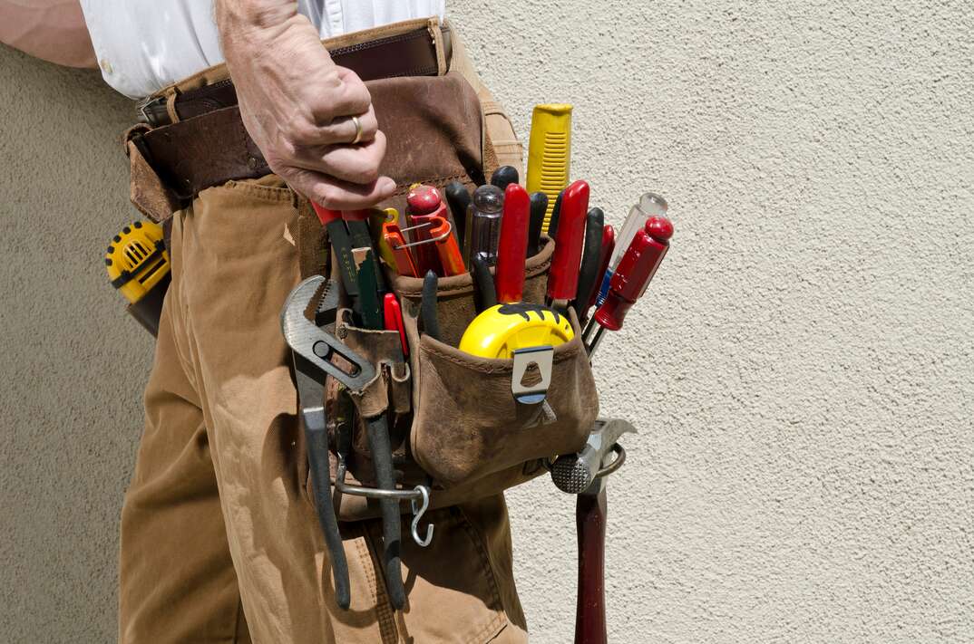 Male handyman with tool belt against stucco wall.