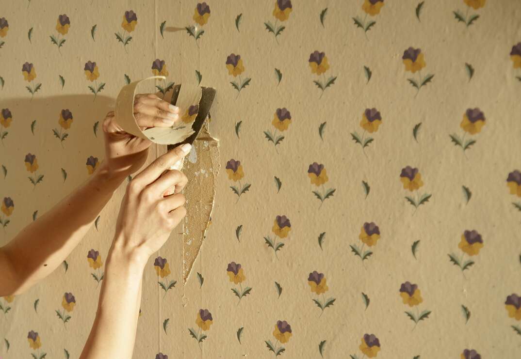 Close up of a hand scraping away wallpaper