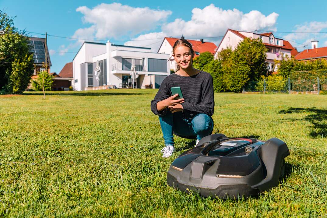 Robotic lawn mower programmed with mobile phone app by a smiling woman
