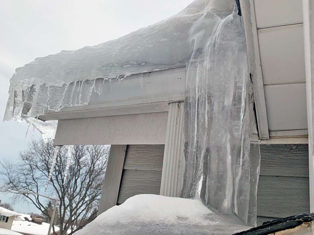 exterior of a home loaded with frozen waterfalls of ice creating a dam on the roof