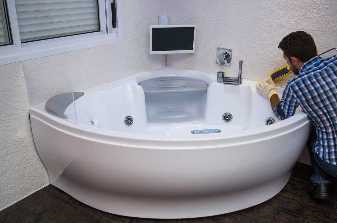 man in a plaid shirt wearing gloves caulking a hot tub that has a television built in above it