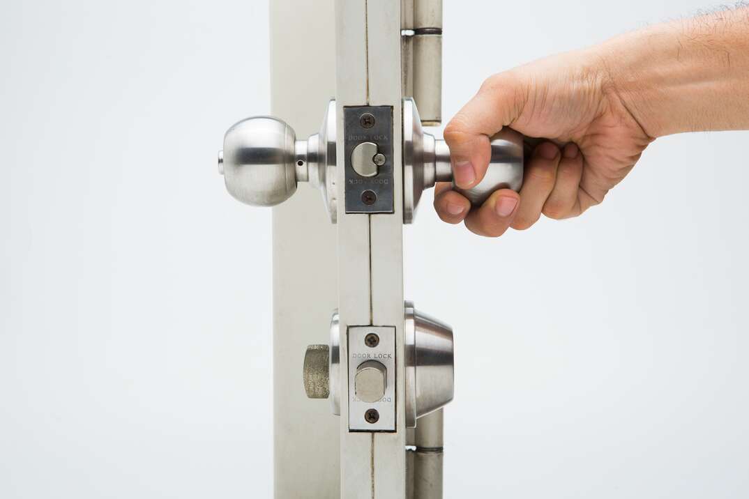 From a side view against a white background person s hand attempts to open a door using the silver metal doorknob