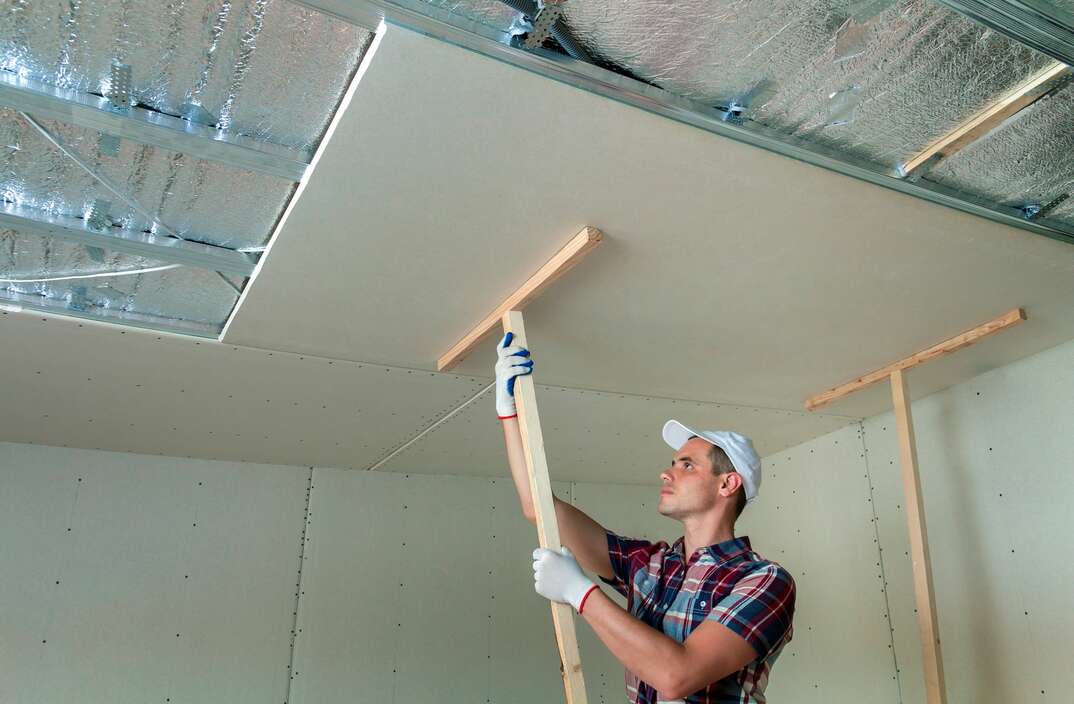 Man in protection work gloves fixing wooden holders for drywall suspended ceiling to metal frame