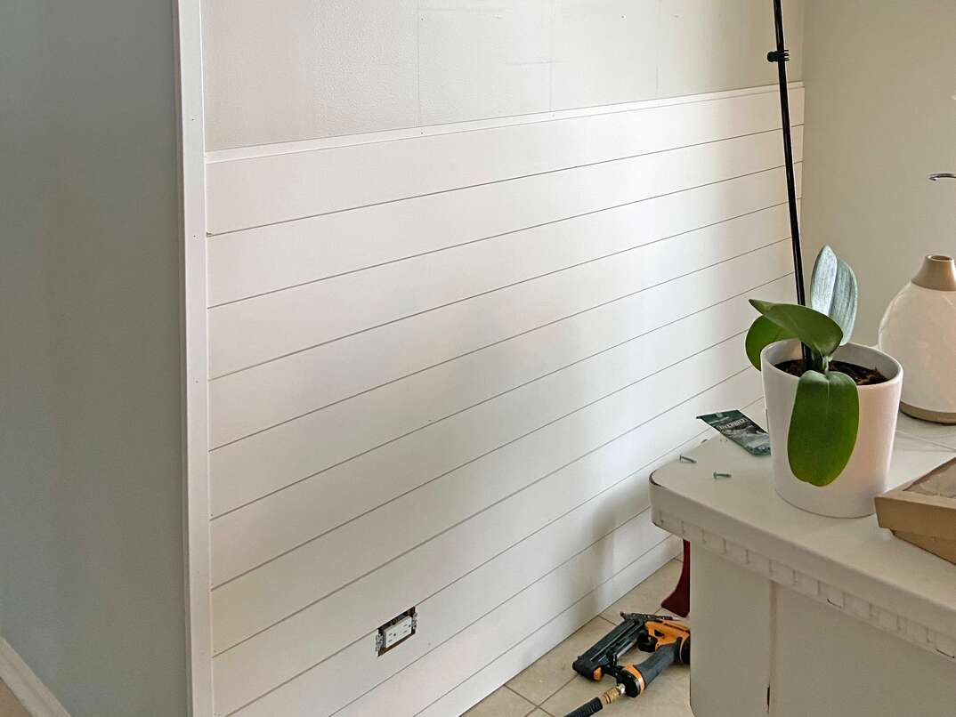 a residential kitchen wall with shiplap being added  The boards go halfway up the wall to show progress  tool lay on the floor 