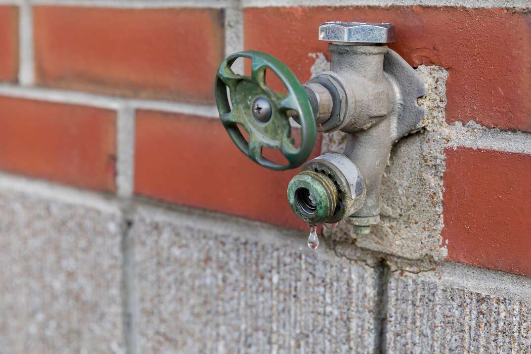 an outside house bib or faucet mounted to a home s brick exterior shown slowly leaking