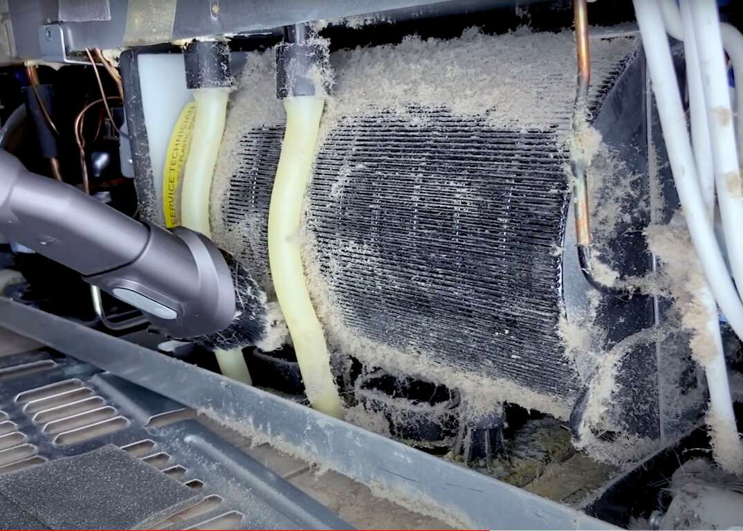 A vacuum cleaner is used to clean the dust and debris off of the condenser coils of a very dirty refrigerator