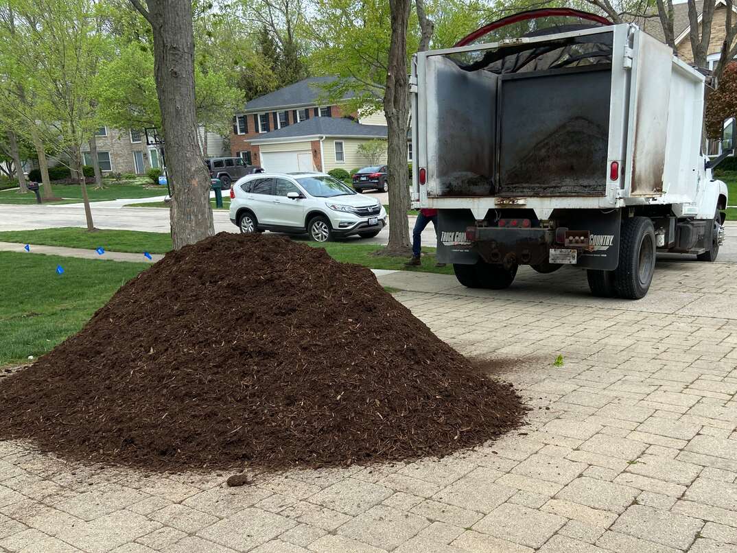 a dump truck delivering hardwood mulch on a residential driveway